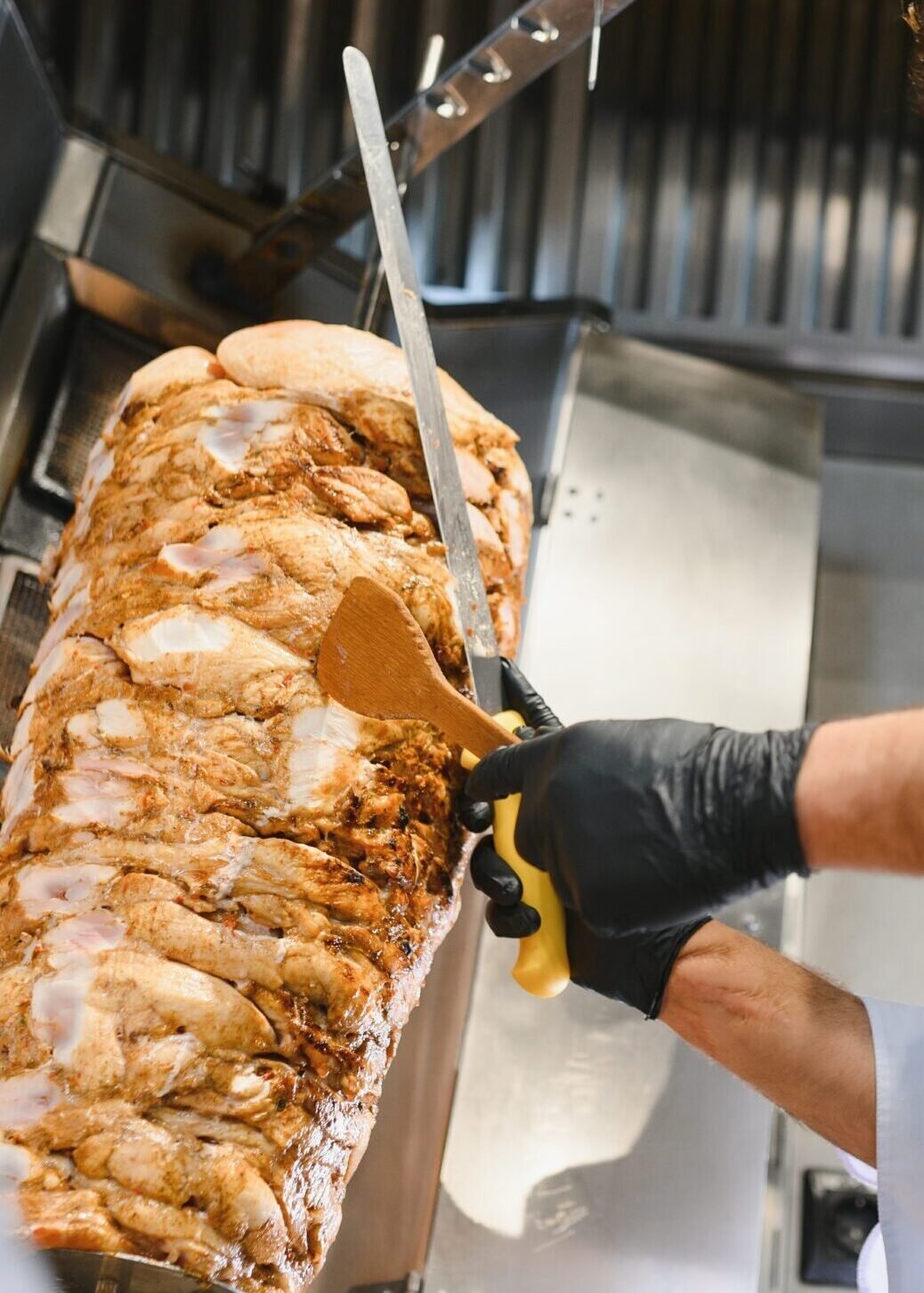 chef slicing shawarma meat on rotating spit in professional kitchen